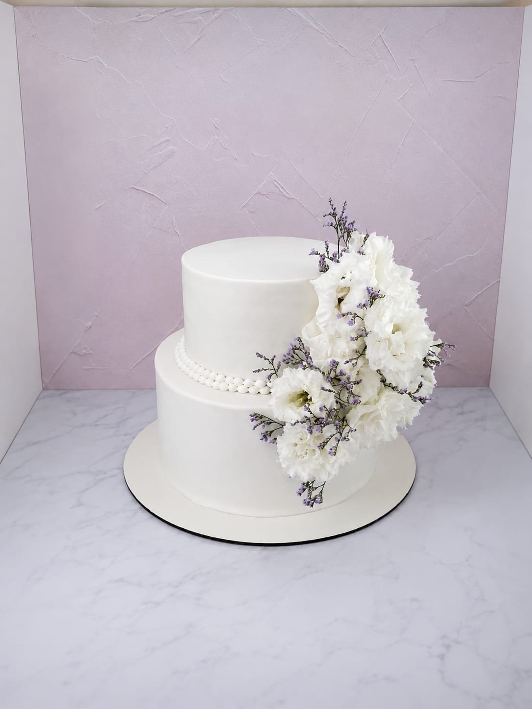 Bolo de casamento branco de dois andares com fio de pérolas e arranjo de flores